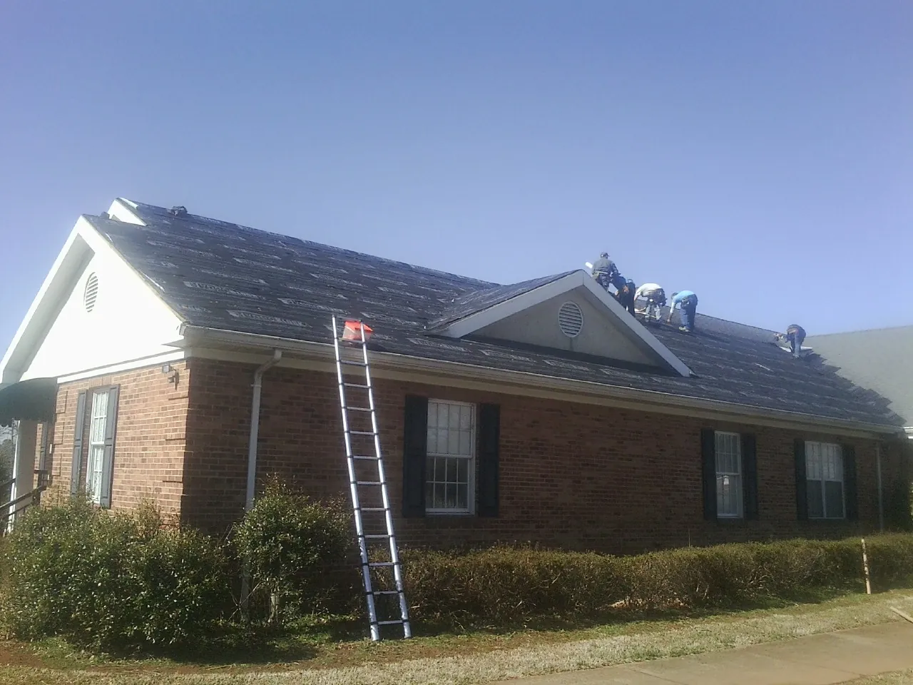Crew tearing shingles off a brick ranch roof with a ladder set — Metal Roof Repair work by our crew in Monsey