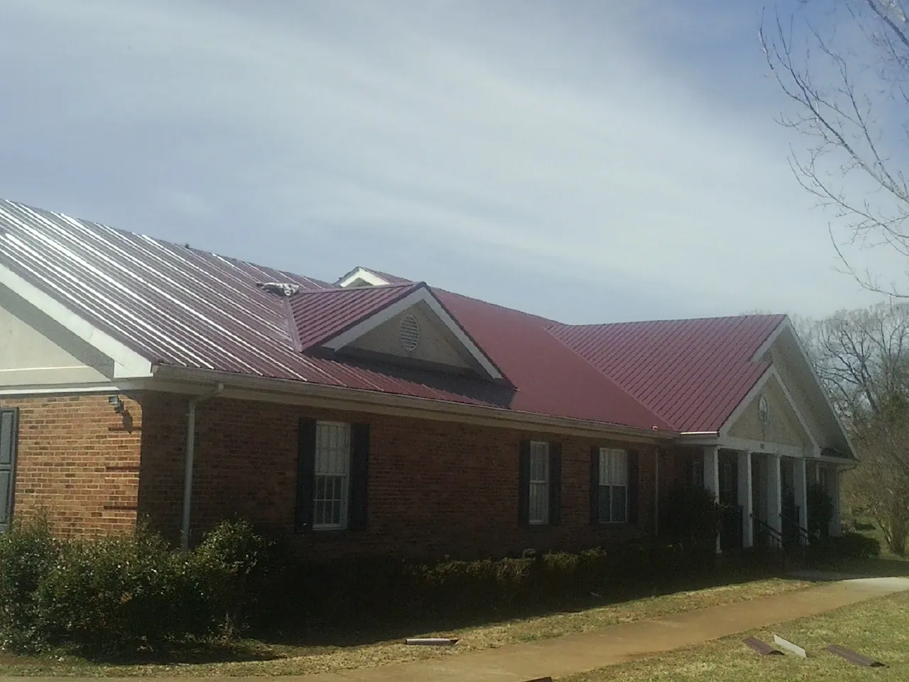 Red metal roof with gabled entries on a long brick building, from a Hail Damage Roof Repair job in Monsey