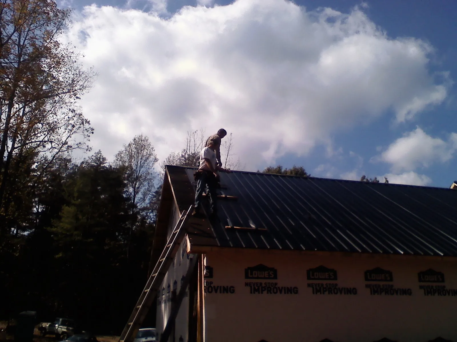 Roofer fastening dark metal panels high against a cloudy sky, from a Roof Inspection job in Monsey