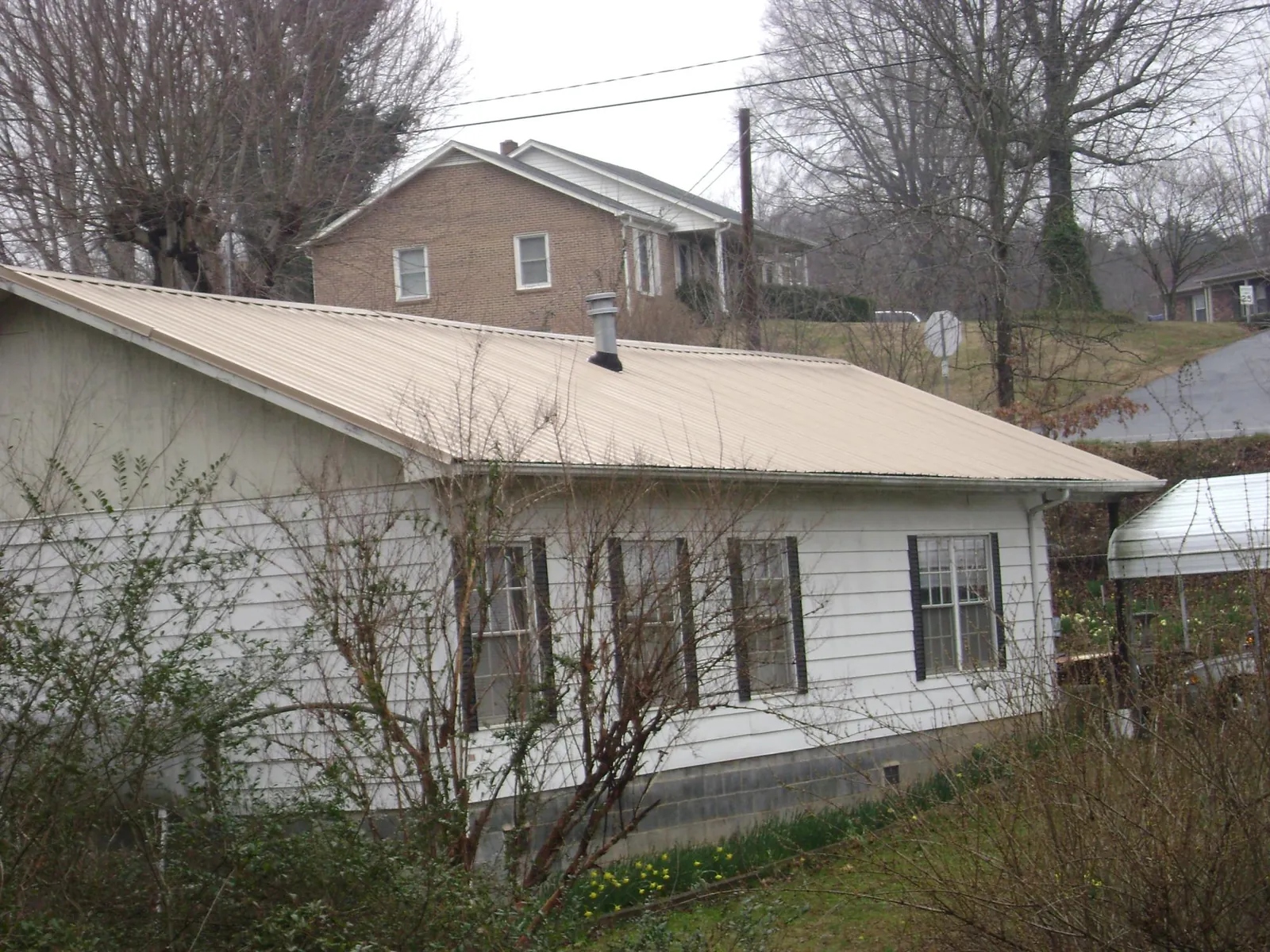 Tan metal roof on a white sided house set into a hillside — Commercial Roofing by Roofing Brothers in Monsey